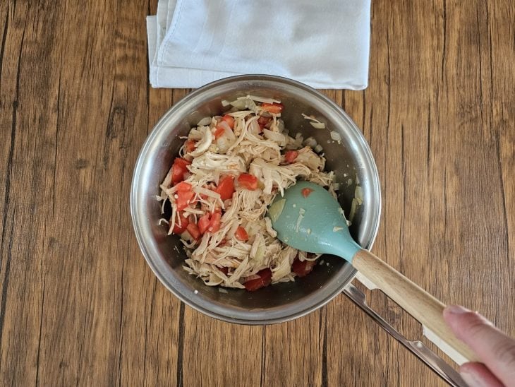 Uma panela contendo frango desfiado e tomate picado.