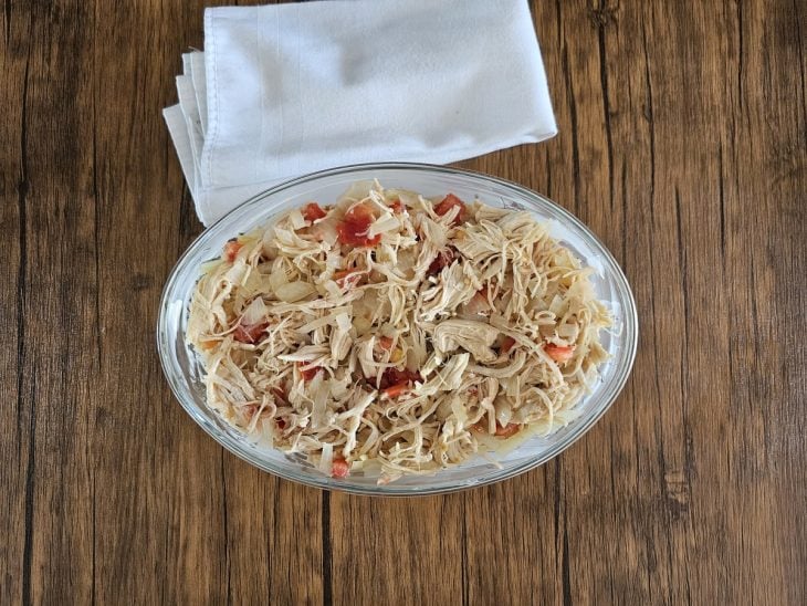 Um refratário forrando com rodelas de batata, cobertas com frango desfiado e tomate.