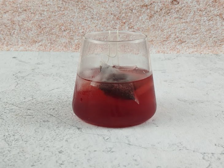 Sachê de chá infusionando em um copo de vidro com água gelada.