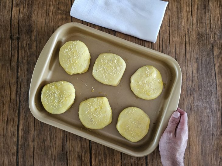 Hambúrgueres de forno pincelados com gema de ovo e salpicados com gergelim.