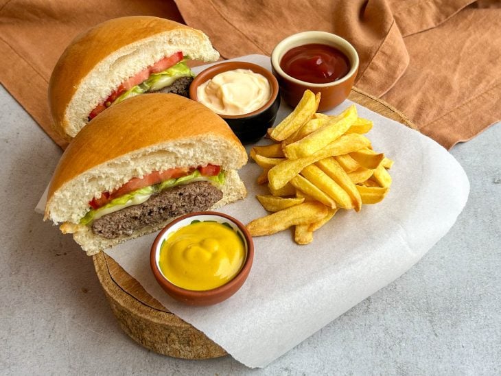 Hambúrguer montado e cortado ao meio, servido com molho e batatas fritas.