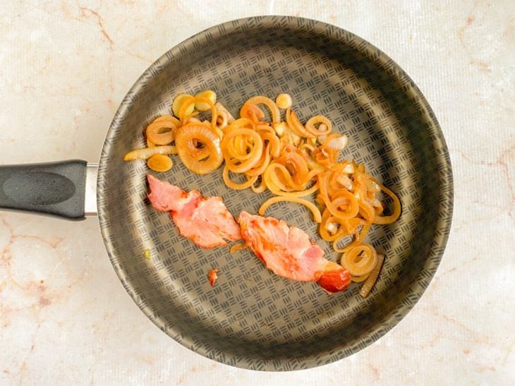 Cebola e bacon fritos em uma frigideira.