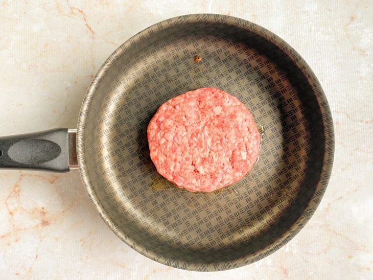 Hambúrguer com um lado temperado colocado no centro da frigideira.