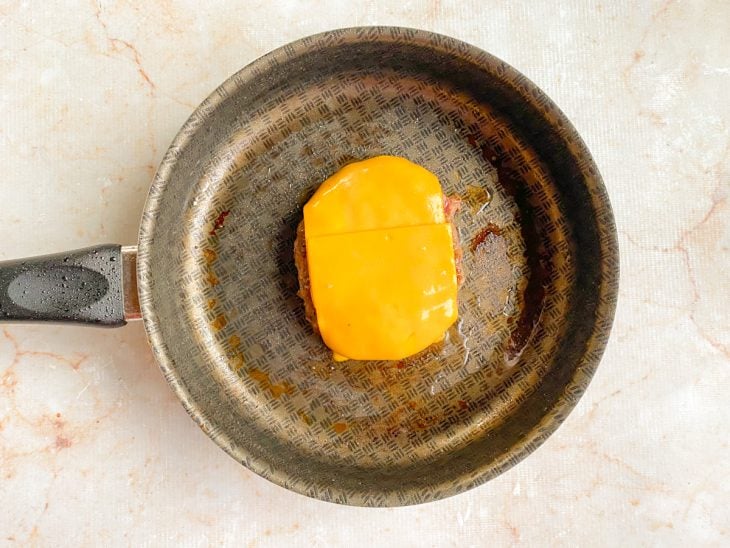 Fatias de queijo colocadas sobre o hambúrguer na frigideira.