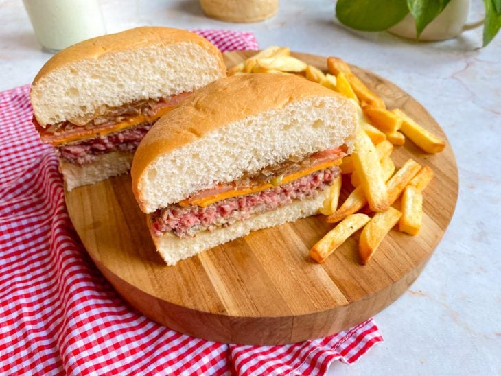 Hambúrguer artesanal fácil e rápido cortado ao meio para consumo e acompanhado por batatas fritas.