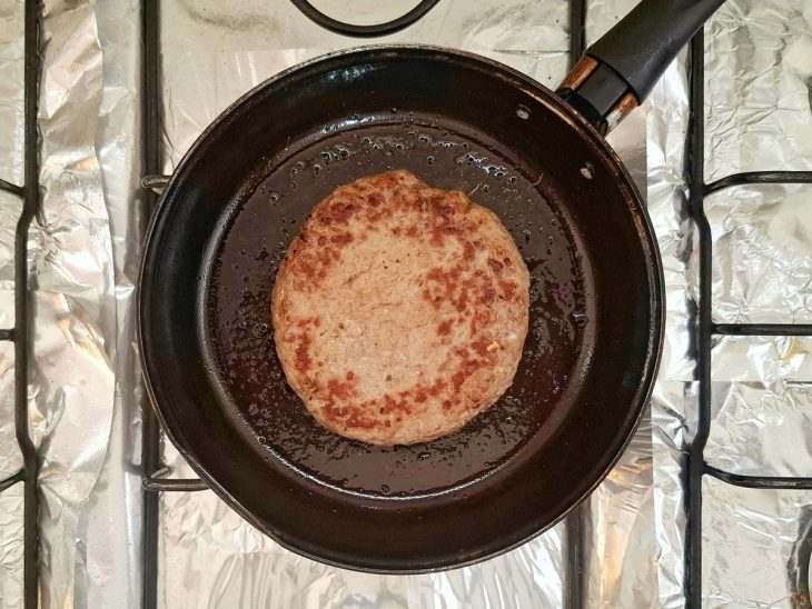 Hambúrguer de carne em uma frigideira com sal e pimenta-do-reino.