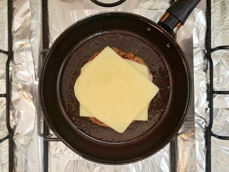 Fatias de queijo adicionadas sobre o hambúrguer na frigideira.