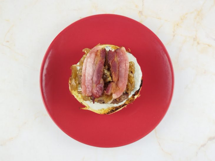 Hambúrguer, cebola caramelizada e o bacon adicionados ao pão.