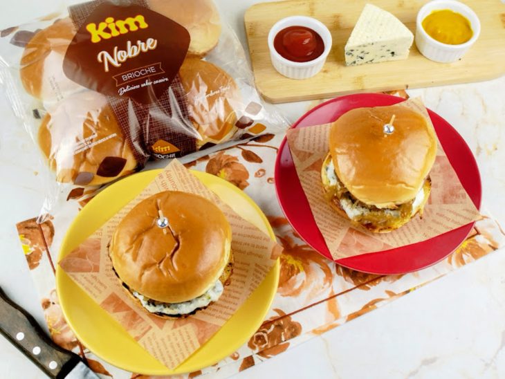 Hambúrgueres prontos, servidos em pratos individuais com molhos.