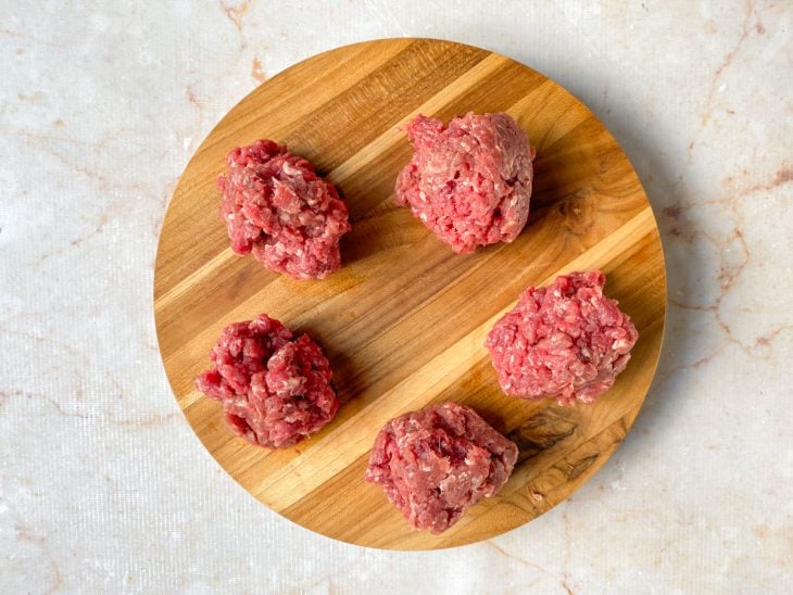 Carne moída separada em 5 porções de 100 gramas sobre uma tábua.