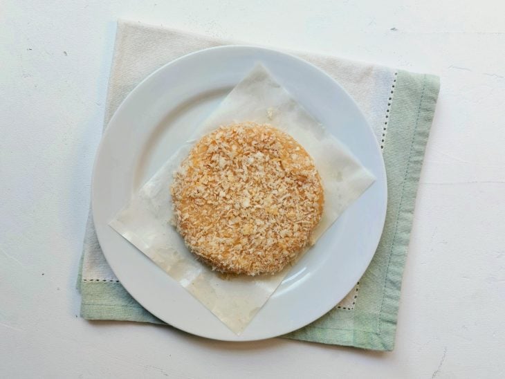 Um hambúrguer cru de frango sendo empanado na farinha de panko.