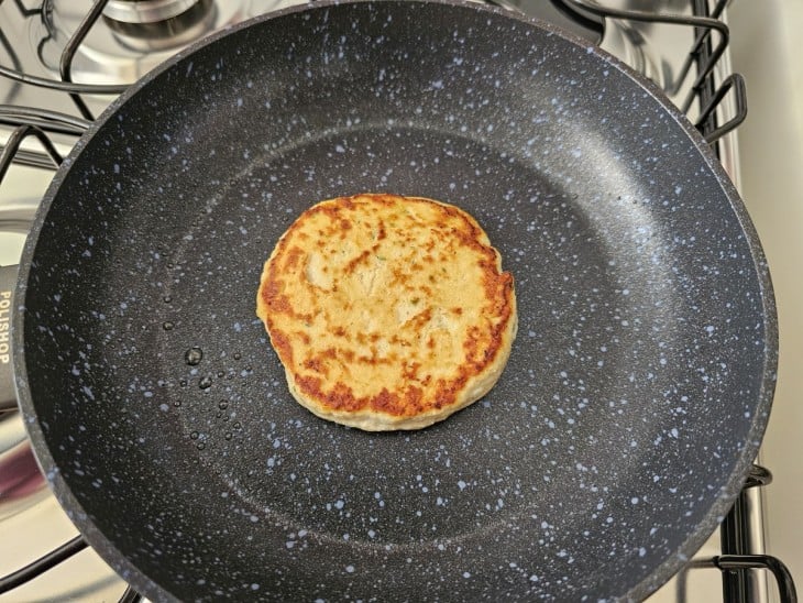 Uma frigideira contendo um sanduíche com hambúrguer de frango fit com aveia sendo frito.