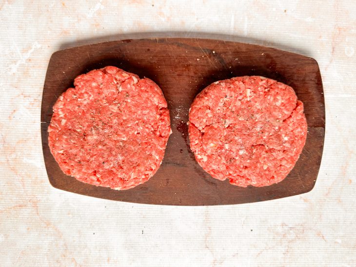 Hambúrguer sendo temperado com sal e pimenta antes de ir à air fryer.
