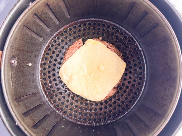 Fatias de queijo sendo colocadas sobre os hambúrgueres já quase prontos.