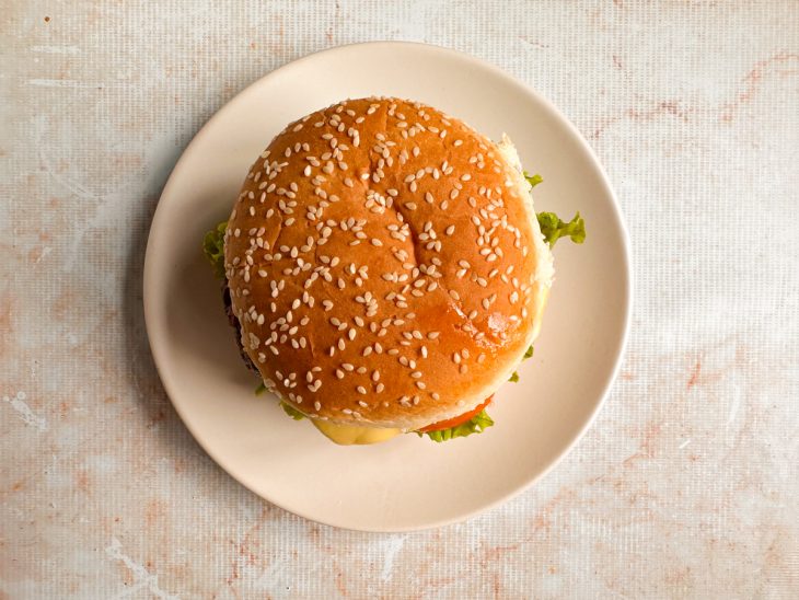Lanche finalizado com alface, tomate, hambúrguer com queijo e pão selado.