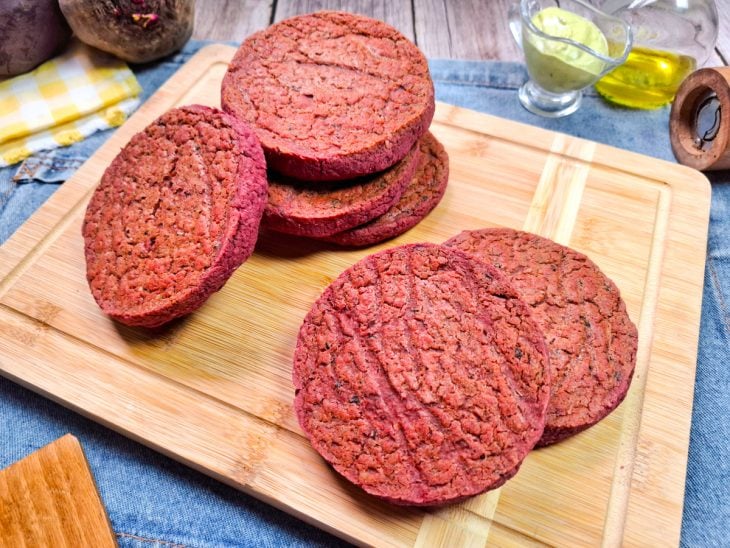 Hambúrgueres vegano de beterraba prontos para consumo servidos sobre uma tábua.