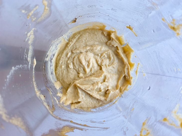 Alho com azeite, grãos-de-bico cozidos, suco do limão, azeite, água do cozimento, sal, pimenta-do-reino e cubo de gelo processados em um liquidificador.