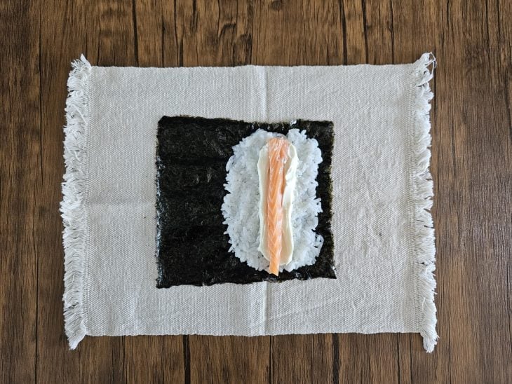 Um pano com folha de nori com uma porção de arroz, cream cheese e uma tira de salmão.