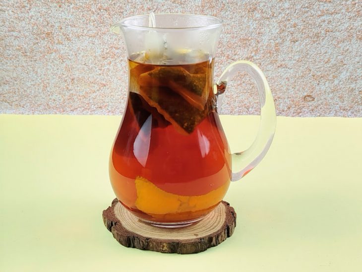 Sachês de chá infusionando em uma jarra de vidro com água e cascas de laranja.