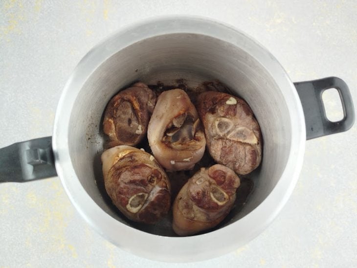 Postas de joelho sendo seladas em panela de pressão com azeite quente.