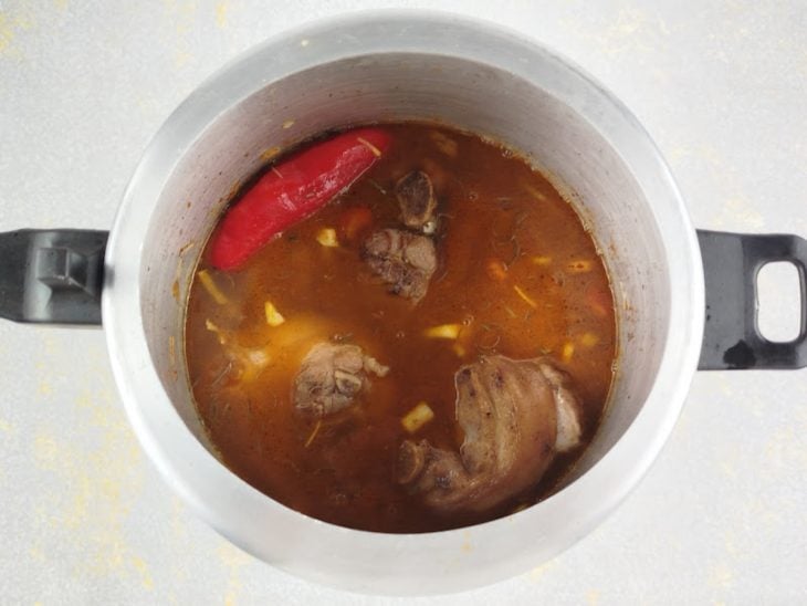 Carne retornando à panela com ervas e sendo coberta com água.