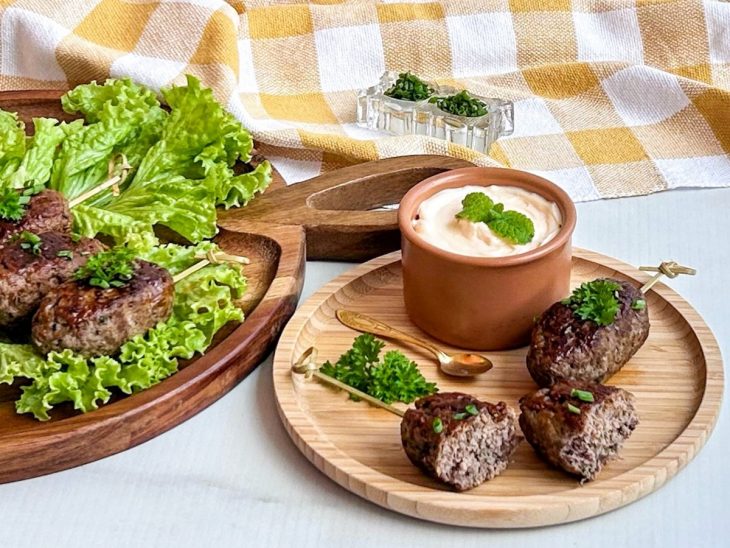 Kaftas prontas ao lado, num prato duas servidas e uma cortada ao meio, com molho acompanhando.