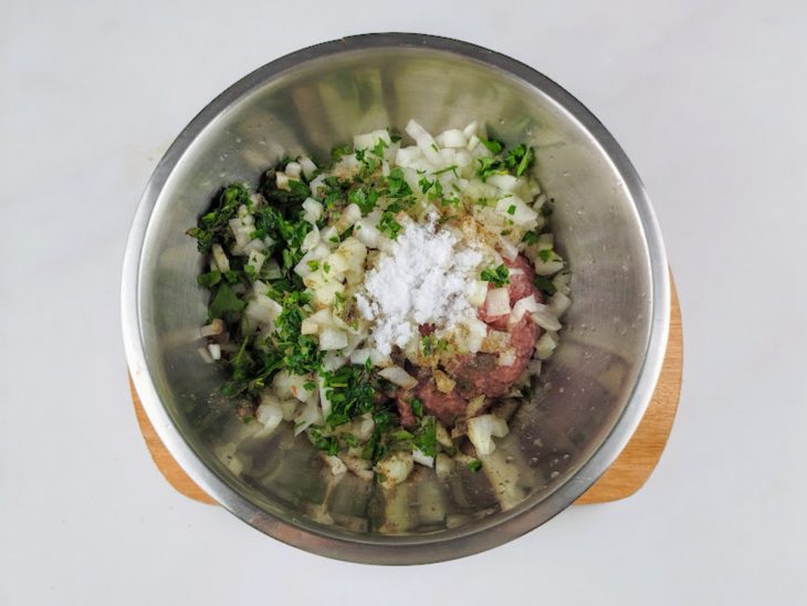 Carne moída, cebola, salsinha, suco de limão, pimenta e sal adicionados em uma tigela.