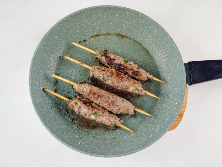 Espetos de kaftas fritando em uma frigideira.