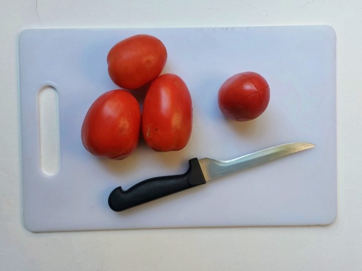 Uma tábua contendo 3 tomates com cortes no topo.