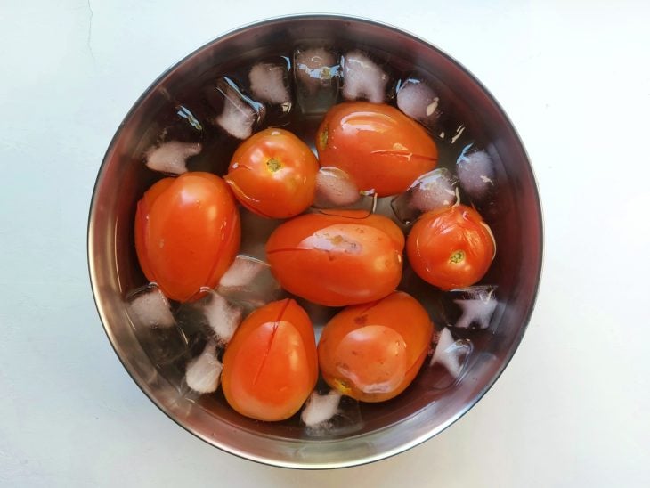 Um recipiente contendo água gelada com gelo e tomates.