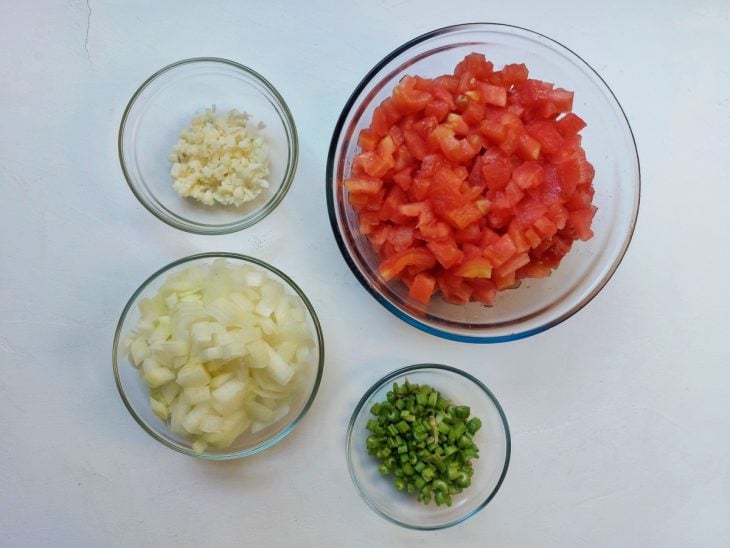 Quatro recipientes contendo em cada tomates picados, talos picados, cebola picadas e alhos picados.