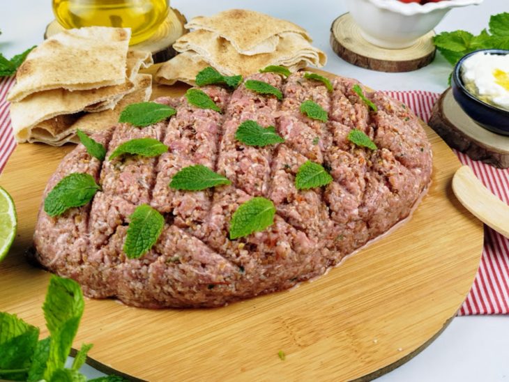 Kibe cru finalizado com folhas de hortelã e servido com pão sírio e coalhada.