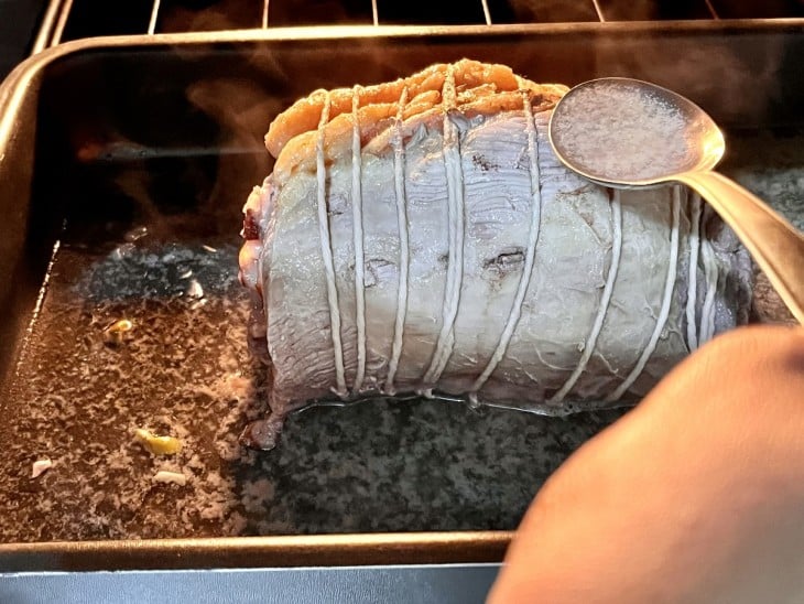 Mão banhando a carne com o caldo de vinho e água.