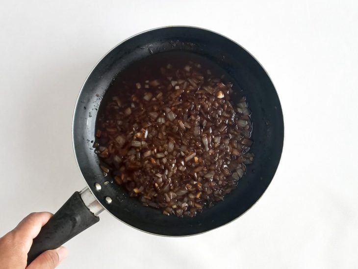 Alho e cebola refogando na frigideira com shoyu, água e sal.