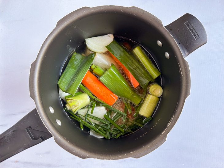 Na panela com a panceta, alho, a cebola, a cenoura, o maço de cebolinha e as folhas de alho-poró adicionados.