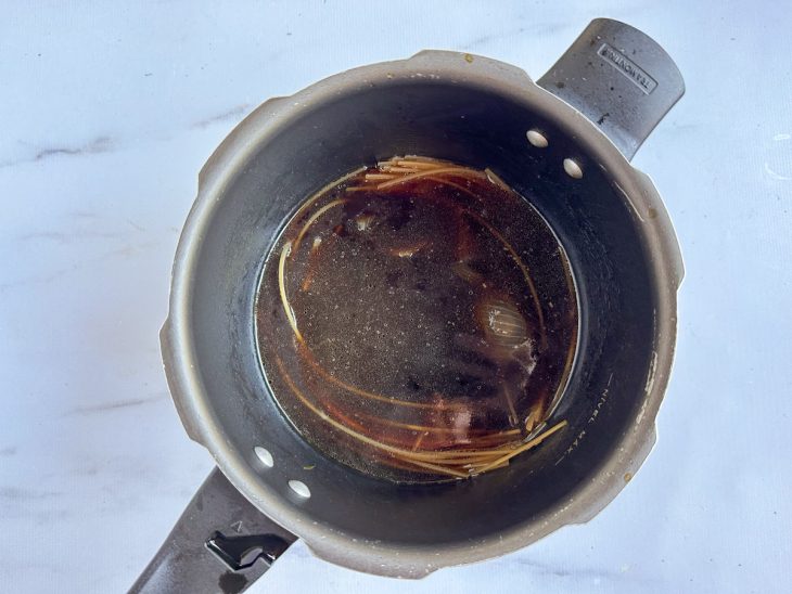 Macarrão disposto na água da panela de pressão, já cozido.