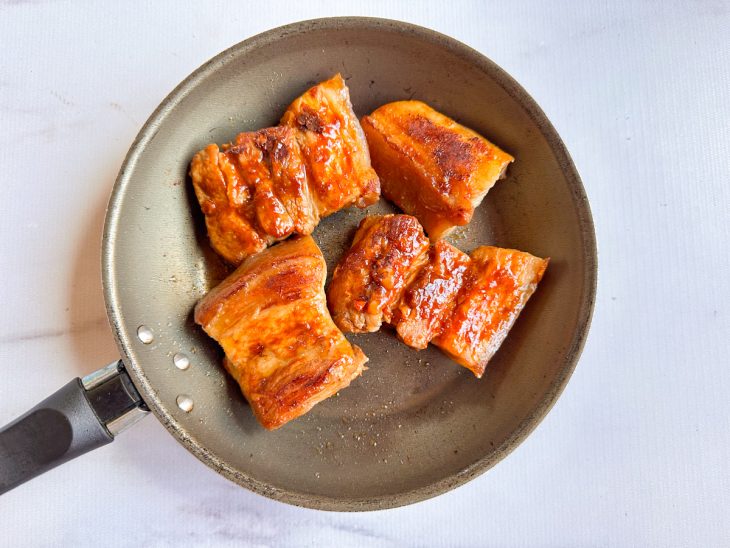 Na frigideira, os pedaços de panceta regados no molho.