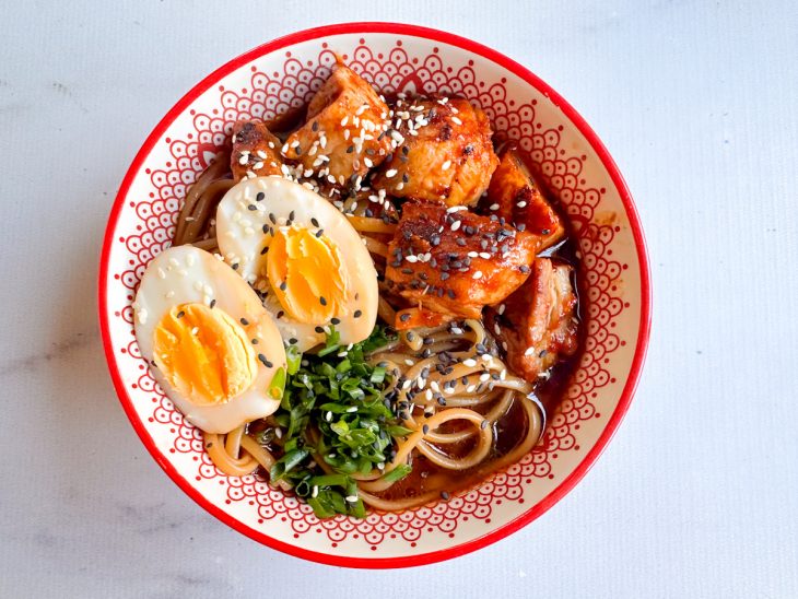 Na tigela, o macarrão, os pedaços de panceta, os ovos, cebolinha verde e o gergelim adicionados.