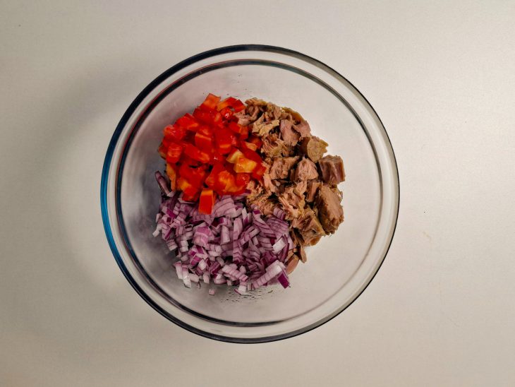 Atum escorrido sendo colocado em uma tigela com tomate e cebola.