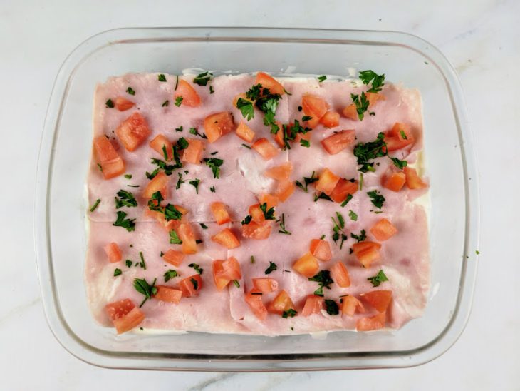 Fatias de presunto, tomate picado e salsinha adicionados na travessa.
