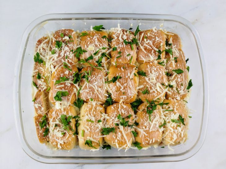 Parmesão e salsinha salpicados sobre as bisnagas na travessa.