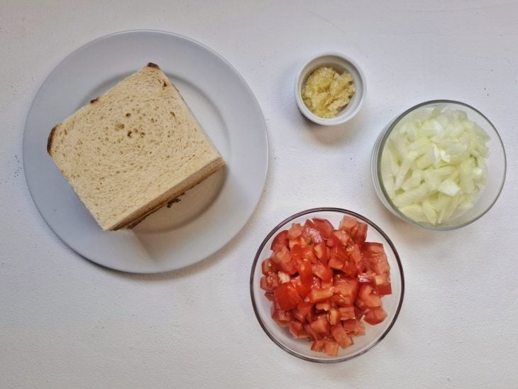 Cebola e alhos descascados e picados, tomate cortado em cubinhos, e pães com as cascas retiradas.