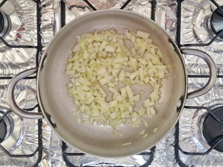Panela ao fogo com alho e cebola sendo refogados.
