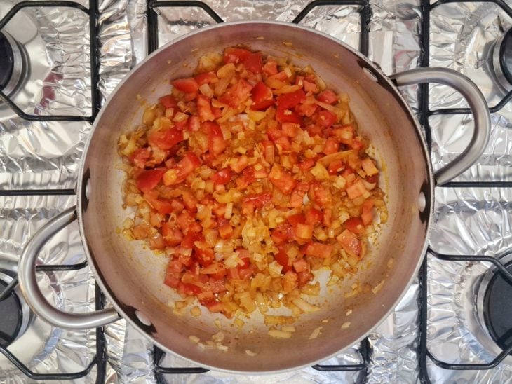 Tomate picado sendo refogado em uma panela ao fogo.