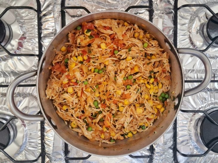Panela com o frango refogado com milho, ervilha e cheiro-verde misturados.