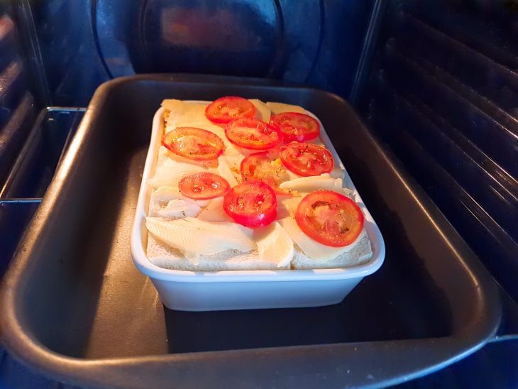 Lanche de forno finalizado com queijo e tomate por cima, dentro do forno.
