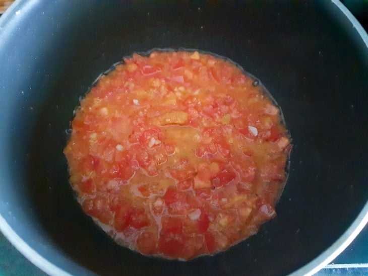 Panela com tomates picados, cebola e alho sendo refogados.
