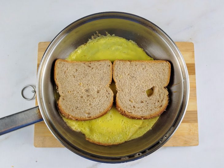 Fatias de pão dispostas na frigideira sobre os ovos.