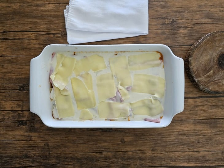 Uma forma forrada com molho bolonhesa coberta com massa de lasanha, molho branco e queijo.