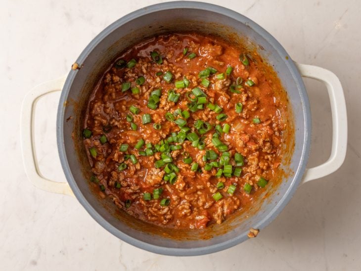 Uma panela com o molho de carne moída finalizado com cheiro-verde.